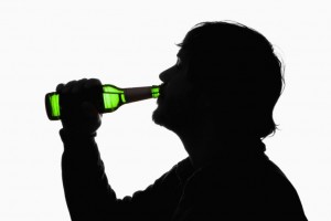 A silhouetted man drinking beer from a bottle